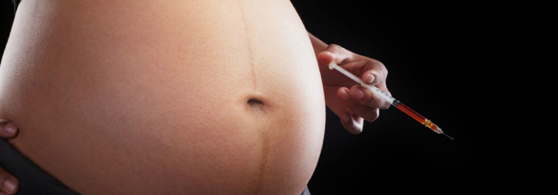 Беременная женщина держит в руках шприц