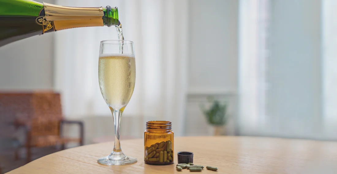 На столе бокал с шампанского и баночка с лекарствами