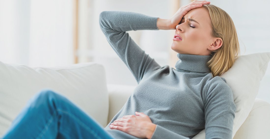 Женщина лежит на диване и держится за живот и голову