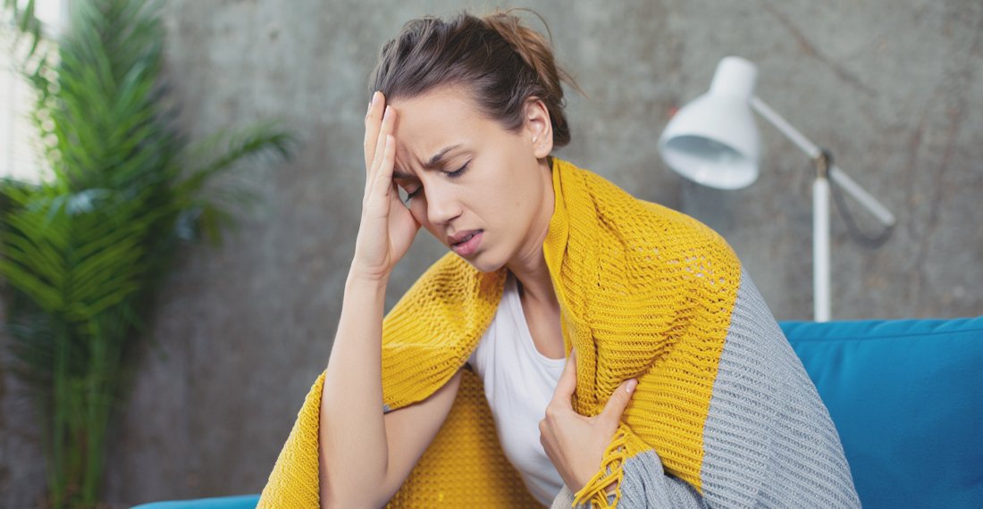 Женщина, укрывшись одеялом, держится за голову