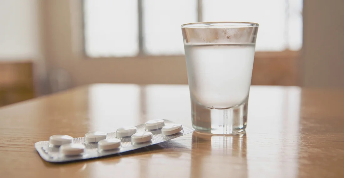 Стопка водки и блистер с таблетками на столе